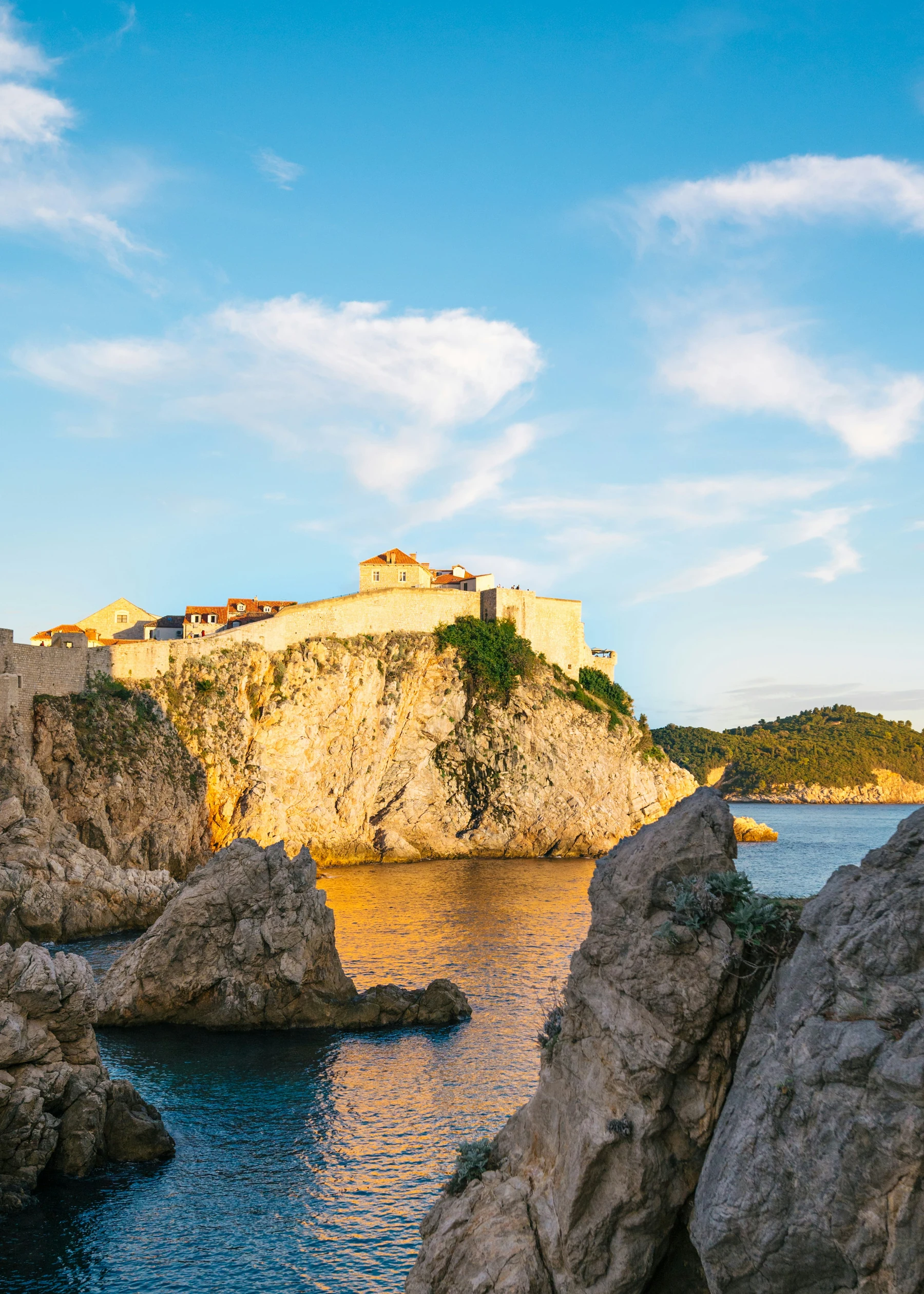 Dubrovnik’s golden stone walls above a rocky Adriatic cove at sunset